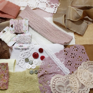 Può includere: Una collezione di materiali per l'artigianato nei toni del rosa, marrone e crema. L'immagine include rocchetti di filo, pizzo, ritagli di tessuto, bottoni e nastri. I materiali sono adatti per cucito, scrapbooking o altri progetti fai-da-te.