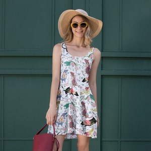 May include: A white sleeveless dress with a floral print featuring colorful cartoon cats. The dress has a fitted bodice and a flared skirt. The model is wearing a straw hat and sunglasses.