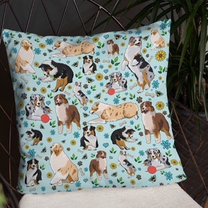 May include: A blue throw pillow with a repeating pattern of Australian Shepherd dogs playing with red balls and bees on a light blue background.