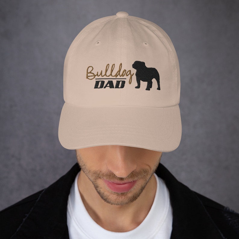 May include: A beige baseball cap with an embroidered black bulldog silhouette and the text "Bulldog DAD" in brown thread.
