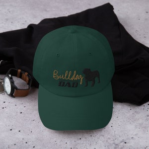 May include: A dark green baseball cap with an embroidered bulldog silhouette and the text "Bulldog Dad" in gold thread.