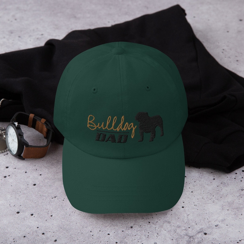 May include: A dark green baseball cap with an embroidered bulldog silhouette and the text "Bulldog Dad" in gold thread.