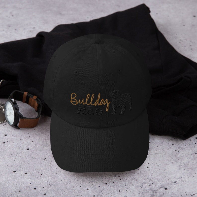 May include: Black baseball cap with a gold embroidered bulldog silhouette and the text "Bulldog Dad".