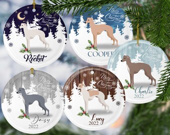 Pode incluir: Conjunto de cinco enfeites de Natal redondos com ilustrações de galgos. Cada enfeite tem um fundo único com uma cena de inverno, as palavras "Merry Christmas" e o nome de um cão. Os nomes são Rocket, Cooper, Charlie, Daisy e Lucy.