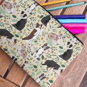 May include: A beige zippered pouch with a repeating pattern of brown, black, and white border collie dogs, green leaves, and gold acorns.