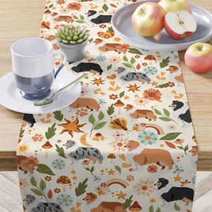 May include: A white table runner with a repeating pattern of colorful flowers, stars, mushrooms, and rainbows.  The pattern also includes a variety of dogs with brown, black, and blue fur.