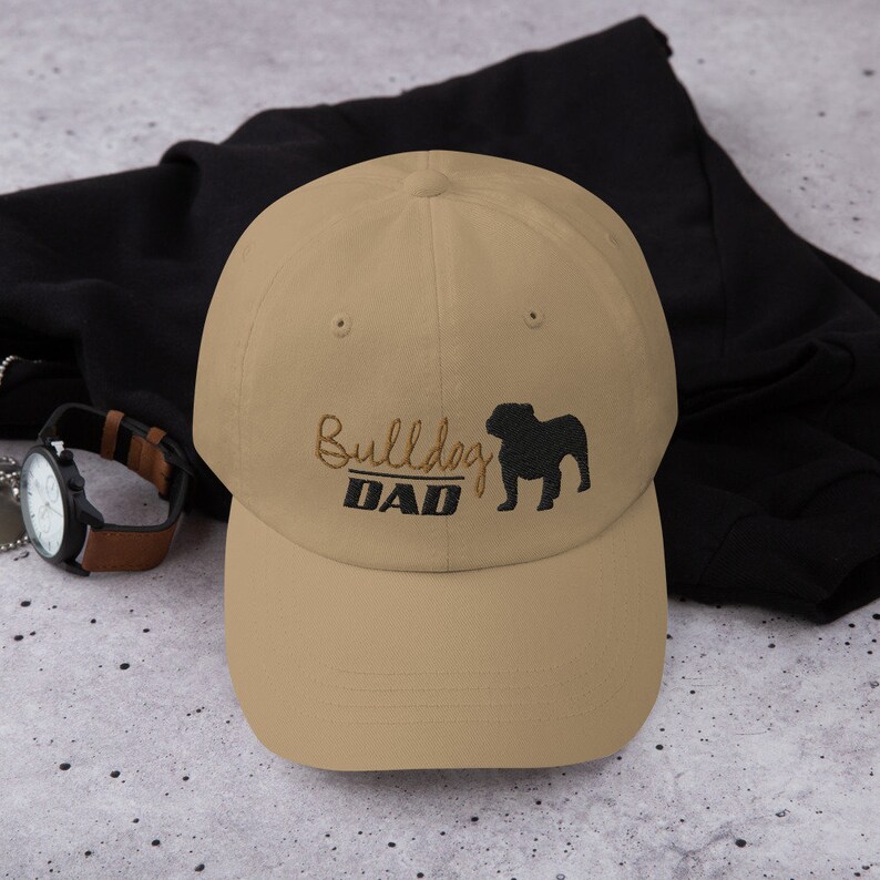 May include: A tan baseball cap with an embroidered black bulldog silhouette and the text "Bulldog DAD".