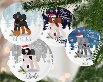 Peut inclure: Quatre boules de Noël rondes représentant un fond blanc avec une scène d'hiver et un caniche portant un bonnet de Père Noël. Chaque boule a un fond de couleur différente et une race de chien différente. Les boules sont étiquetées avec les noms "Blacky", "Reggie", "Drake" et "Merlin".