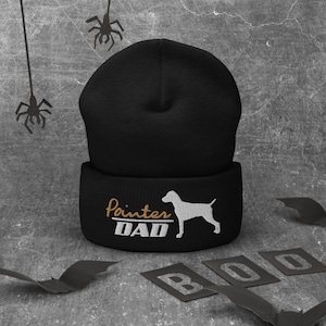 May include: Black knit beanie with a white silhouette of a dog and the text "Pointer Dad" in gold embroidery.