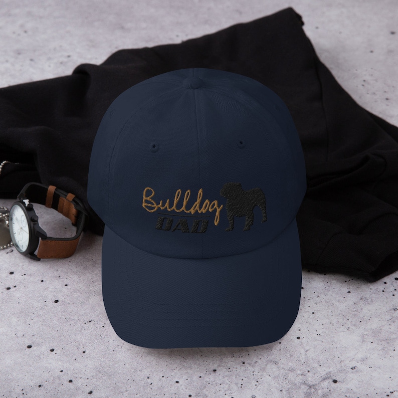 May include: A navy blue baseball cap with an embroidered bulldog silhouette and the text "Bulldog Dad" in gold thread.