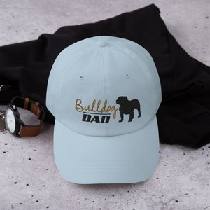 May include: A light blue baseball cap with a black bulldog silhouette and the text "Bulldog Dad" embroidered in gold thread.