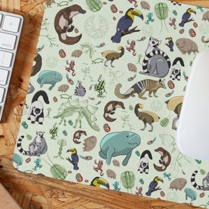 Pode incluir: Um tapete de rato verde com um padrão repetido de vários animais, incluindo um ornitorrinco, um tucano, um lêmure, um peixe-boi e um dinossauro. Os animais são desenhados em estilo de desenho animado e são cercados por vários outros elementos, como folhas, flores e fósseis.