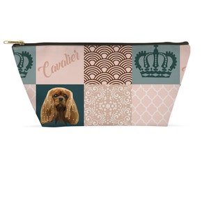 Pode incluir: Uma bolsa de cosméticos com zíper e design de patchwork. A bolsa apresenta uma ilustração de Cavalier King Charles Spaniel, coroas e padrões geométricos em verde-azulado, rosa e castanho. A palavra "Cavalier" está impressa.