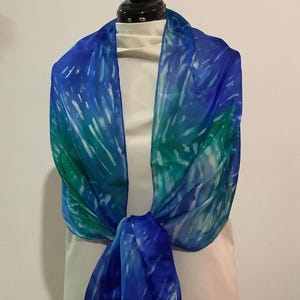 May include: A blue and green silk scarf with a tie-dye pattern. The scarf is tied around a white mannequin's neck.