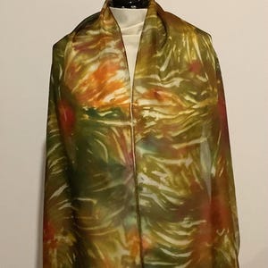 May include: A long, flowing silk scarf with a hand-painted abstract design in shades of green, orange, and white.