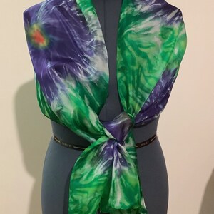 May include: A green and purple silk scarf with a tie-dye pattern. The scarf is tied around a dress form.