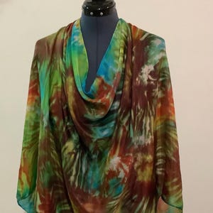 May include: A colorful, tie-dye scarf draped over a mannequin. The scarf features a blend of green, blue, brown, and red hues. The fabric appears lightweight and flowing, with a pattern that resembles a watercolor painting. The scarf is a fashion accessory.