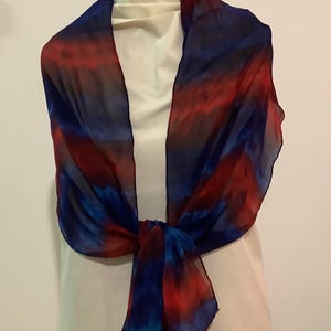 May include: A blue and red silk scarf with a tie-dye pattern. The scarf is tied around a white mannequin's neck.