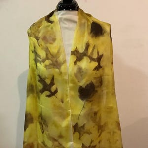 May include: A rectangular scarf featuring a vibrant yellow base color with dark brown botanical leaf imprints scattered across the fabric. The scarf displays a variety of distinct leaf shapes and sizes, creating a natural pattern throughout the material.