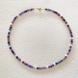 Könnte beinhalten: Eine mehrfarbige Perlenkette mit blauen, rosa und weißen Perlen. Die Kette besteht aus Edelsteinperlen und ist auf einer goldenen Kette aufgefädelt.