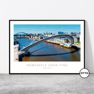 Può includere: Una stampa incorniciata con una vista panoramica di Newcastle upon Tyne, in Inghilterra. L'immagine mostra un moderno ponte pedonale bianco che si inarca su un fiume, con lo skyline della città sullo sfondo sotto un cielo blu.