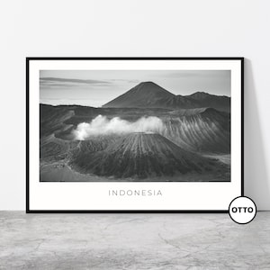 Può includere: Fotografia in bianco e nero di un paesaggio vulcanico in Indonesia. L'immagine mostra un grande vulcano attivo con fumo che fuoriesce dal suo cratere. Il vulcano è circondato da colline e montagne più piccole, e il cielo è nuvoloso.