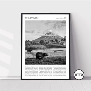 May include: Black and white framed print featuring a landscape of the Philippines. The image shows a volcano in the background, with cows grazing in a field in the foreground. The word "PHILIPPINES" is printed at the top.