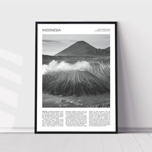 Op de afbeelding: Zwart-wit ingelijste print met een vulkanisch landschap in Indonesië. De afbeelding toont een grote vulkaan met een krater en een kleinere berg op de achtergrond. Het woord "INDONESIA" staat bovenaan afgedrukt.