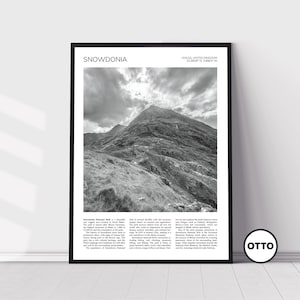 May include: Monochrome framed print of the Snowdonia mountain range in Wales. The print displays the word "SNOWDONIA" and coordinates. The image shows a rugged mountain landscape under a cloudy sky, with text at the bottom.