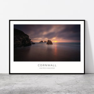 May include: A scenic photograph of a rocky coastline in Cornwall, United Kingdom. The image features a dramatic sunset with a cloudy sky and a calm ocean. The sun is setting behind the horizon, casting a warm glow over the water. The rocks are silhouetted against the sky, creating a sense of mystery and beauty.