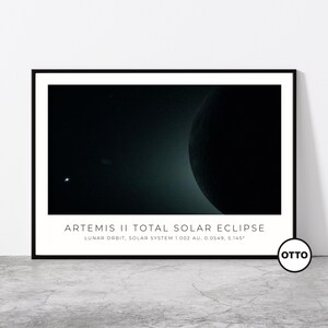 May include: A framed print featuring a dark image of a total solar eclipse. The image shows a dark planet with a bright light source and text that reads "ARTEMIS II TOTAL SOLAR ECLIPSE". The print is in a black frame.