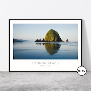 May include: A photograph of Cannon Beach in Oregon, USA. The image shows a large rock formation, Haystack Rock, covered in green vegetation, with its reflection in the calm water. The sky is a light blue with a few clouds.