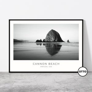 Peut inclure: Tirage encadré en noir et blanc de Cannon Beach, Oregon, USA. L'image présente une grande formation rocheuse dans l'océan, avec son reflet visible dans le sable mouillé. Le texte "Cannon Beach, Oregon, USA" est imprimé en bas.