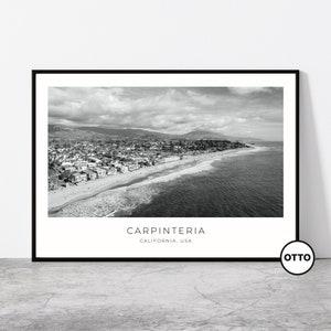 May include: Black and white aerial photograph of Carpinteria, California, USA. The photo shows a beach with waves crashing on the shore, a town with houses and streets, and mountains in the background.