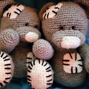May include: Two grey crocheted teddy bears with white patches and black accents. The bears have black button eyes and white noses.