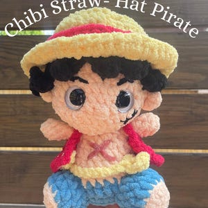 Op de afbeelding: Een gehaakte knuffelpop in de vorm van een Chibi-piraat met strooien hoed, zwart haar, een gele hoed met rode band, een rood vest en een blauwe broek. De pop heeft grote zwarte ogen en een rood X-vormig litteken op de borst. Tekst: *Pattern ONLY*.
