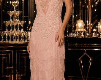 May include: A knee-length, light pink sleeveless dress featuring a V-neckline, intricate beadwork in swirling patterns on the bodice, and multiple tiers of long, delicate fringe extending from the waist down to the hemline.