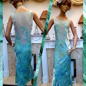 May include: A sleeveless, floor-length dress with a blue and green tie-dye pattern and gold embroidery. The dress has a scoop neck and a fitted silhouette.