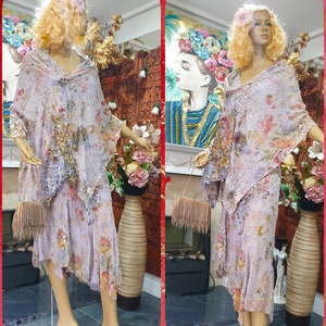 Op de afbeelding: Een lila jurk met bloemenprint en een bijpassend jasje. De jurk heeft een zwierige rok en het jasje heeft een shawlkraag. De mannequin draagt witte schoenen.