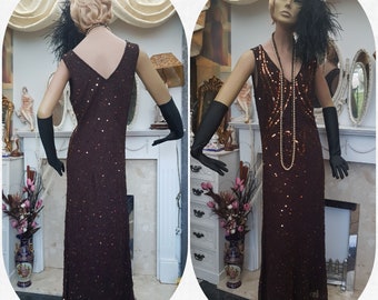 May include: A long, sleeveless, sequined dress in a deep burgundy color with a V-neckline. The dress is adorned with small, iridescent sequins and has a beaded necklace.