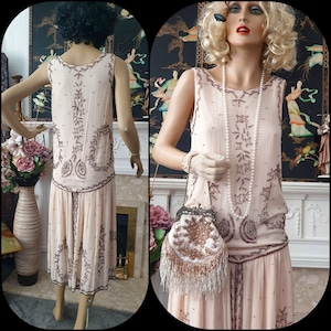 May include: A light pink vintage dress with detailed brown beading and a matching beaded purse. The dress has a sleeveless design, a drop waist, and a pleated skirt. The purse features a beaded design and fringe.