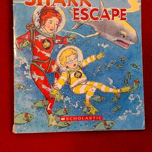 May include: The Magic School Bus Chapter Book #7: The Great Shark Escape. A colorful book cover featuring two children in scuba gear, a shark, and various fish.