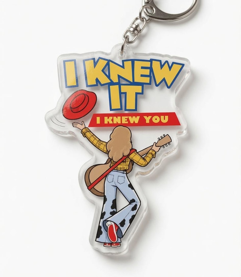 May include: A clear acrylic keychain featuring a cartoon illustration of a person with long hair wearing a yellow plaid shirt and cow-print bell-bottom pants, holding a guitar. The text reads I KNEW IT and I KNEW YOU, with a red hat graphic.