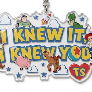 May include: A clear acrylic keyring featuring the text I KNEW IT, I KNEW YOU in yellow with blue outlines. The design includes illustrations of Woody, Buzz Lightyear, Rex, Jessie, Bullseye, and Hamm, along with a rocket, clouds, stars, and a red heart with TS.