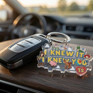 May include: A clear acrylic keyring featuring the text I KNEW IT, I KNEW YOU in yellow letters, surrounded by colourful cartoon character illustrations including a cowboy, a space ranger, a pig, a horse, and a cowgirl, with a red heart labelled TS.