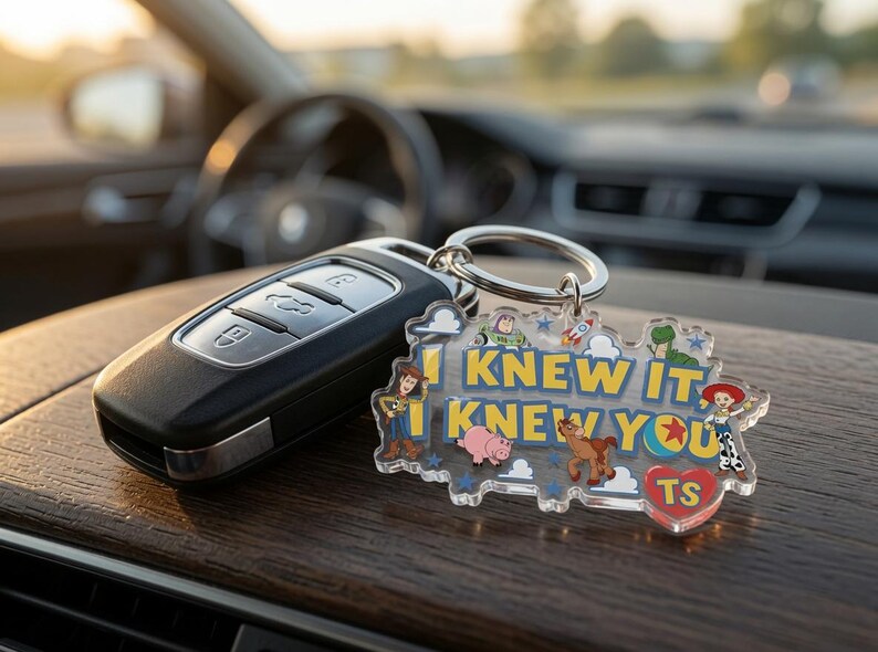 May include: A clear acrylic keyring featuring the text I KNEW IT, I KNEW YOU in yellow letters, surrounded by colourful cartoon character illustrations including a cowboy, a space ranger, a pig, a horse, and a cowgirl, with a red heart labelled TS.