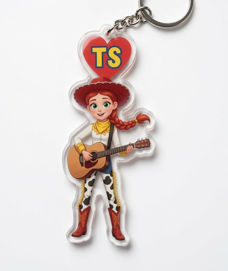 May include: An acrylic keyring featuring a cartoon cowgirl with red hair in a braid, wearing a red hat, white shirt, and cow-print trousers, playing an acoustic guitar. Above her is a red heart with the yellow letters TS printed inside.