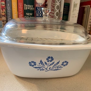 May include: White casserole dish with a clear glass lid. The dish features a blue floral design on the front. The lid has a silver metal handle. A classic piece for baking and serving.