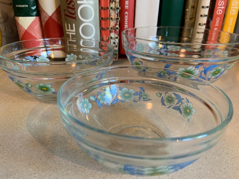 May include: Three clear glass bowls with a floral design. The bowls have a blue and green floral pattern with white accents.