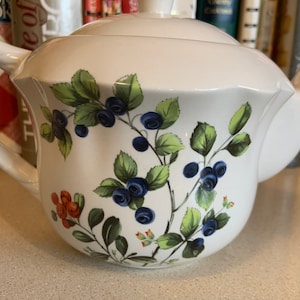 Pode incluir: Bule de chá de cerâmica branca com um design floral com bagas azuis e vermelhas e folhas verdes.